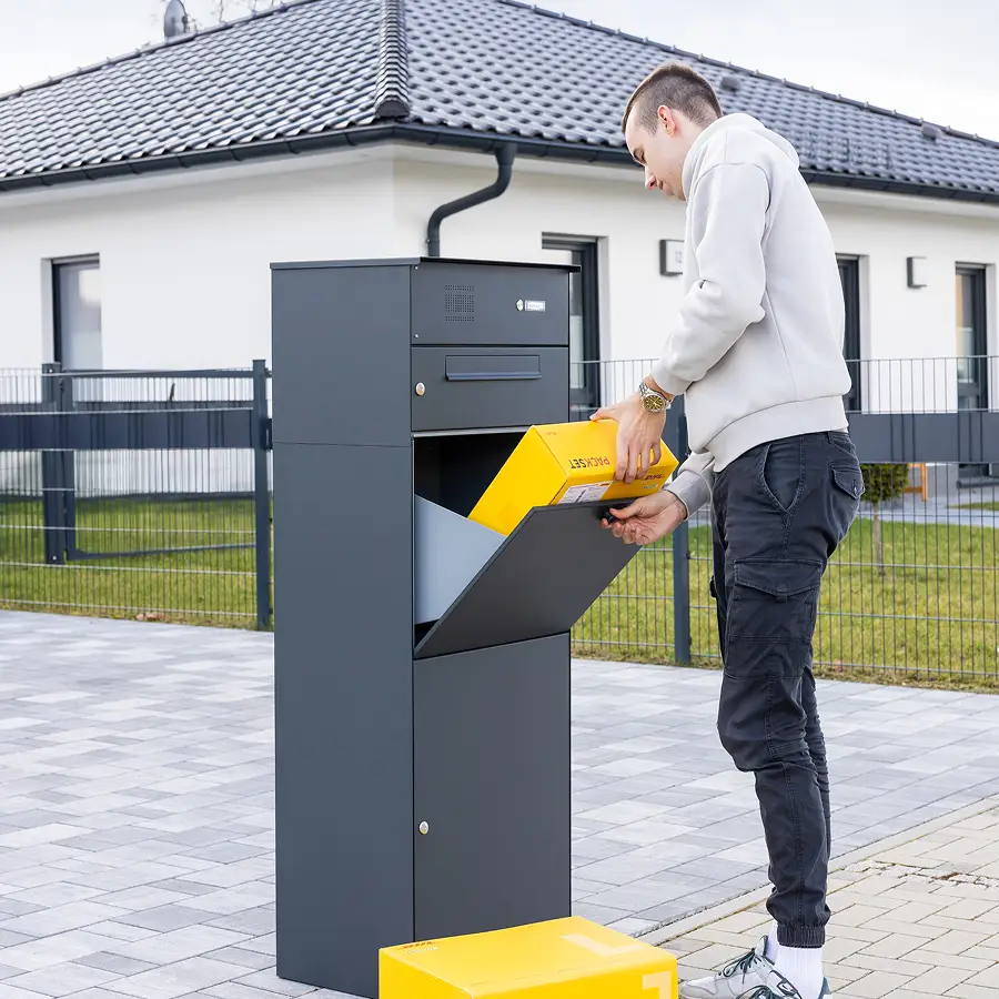 Ein Junger Mann legt ein DHL Paket in der Größe L in die Paketbox KNOBOX PRO 12 mit Briefkasten und Klingel Sprechanlage