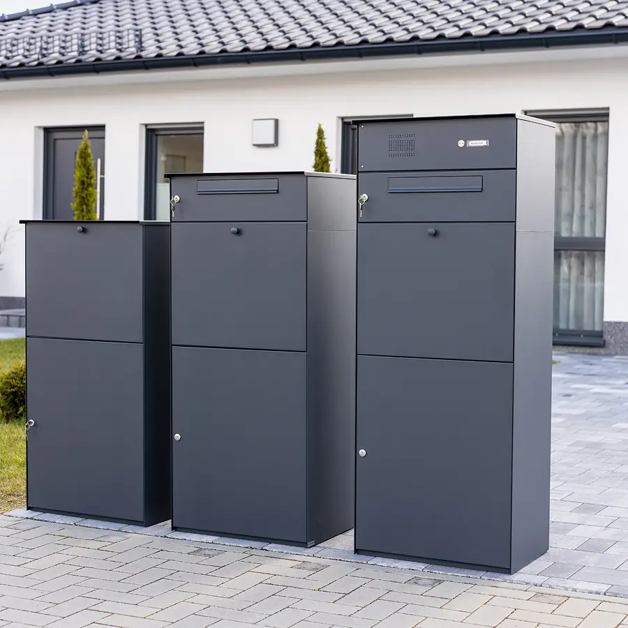 Die Paketbox Serie KNOBOX PRO (Varianten 10, 11 und 12) v.l.n.r. nebeneinander in der Farbe Anthrazit vor einem Einfamilienhaus